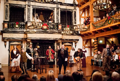 In a theater decked in wreaths and evergreen garland, the cast sings and plays instruments under chandeliers with the audience on three sides.