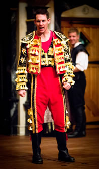 Blunt in bright red and yellow and black matadors waistjack and vest, with tassles hangking off, oversized red pants with black and yellow tassled piping, black boots and red undershirt.